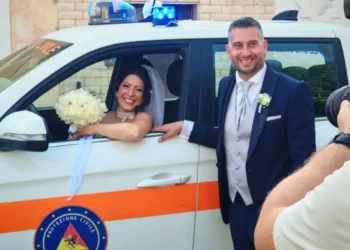 Sposi in posa accanto a un mezzo della Protezione Civile: la sposa al finestrino con bouquet, lo sposo in abito blu.