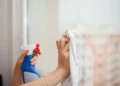 Mani che puliscono un vetro con panno in microfibra dopo aver spruzzato un detergente