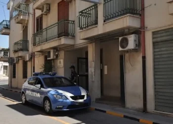 Auto della Polizia di Stato parcheggiata davanti all'ingresso del Commissariato di Comiso, con agente in divisa sul portone