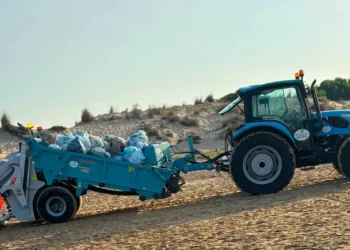 Trattore con mezzo raccoglitore raccoglie sacchi di rifiuti sulla spiaggia di Marina di Modica tra le dune.