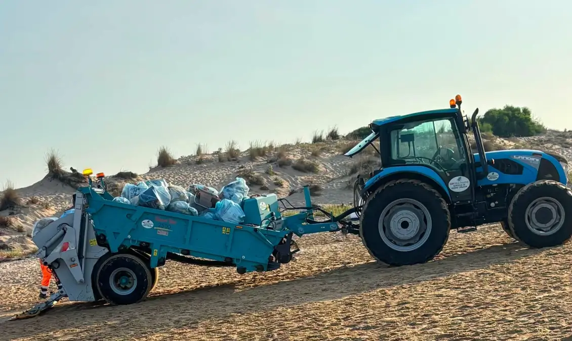 Trattore con mezzo raccoglitore raccoglie sacchi di rifiuti sulla spiaggia di Marina di Modica tra le dune.