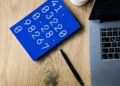 Tavola blu con numeri disposti in sequenza, accanto a laptop, penna e simbolo matematico su una scrivania.