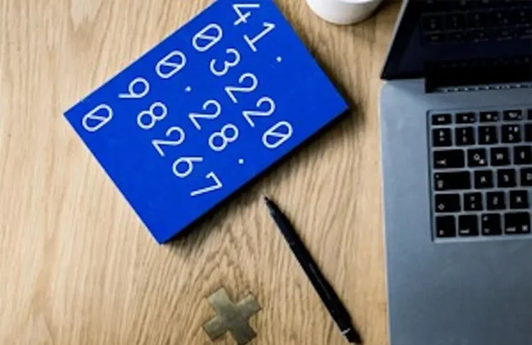 Tavola blu con numeri disposti in sequenza, accanto a laptop, penna e simbolo matematico su una scrivania.