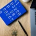 Tavola blu con numeri disposti in sequenza, accanto a laptop, penna e simbolo matematico su una scrivania.