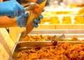 Mani con guanti servono pesce fritto in un cartoccio durante una preparazione gastronomica.