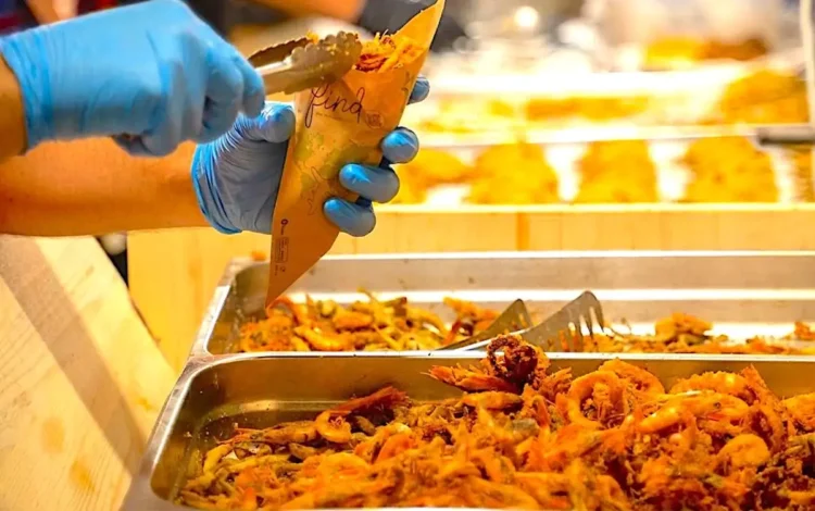 Mani con guanti servono pesce fritto in un cartoccio durante una preparazione gastronomica.