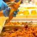 Mani con guanti servono pesce fritto in un cartoccio durante una preparazione gastronomica.