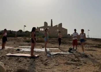 Gruppo di persone su tappetini da yoga davanti alle rovine della Fornace di Punta Pisciotto a Sampieri, Scicli