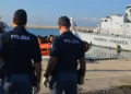 Agenti della Polizia di Stato osservano un'unità della Guardia di Finanza e un gommone con migranti in banchina al porto
