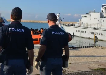 Agenti della Polizia di Stato osservano un'unità della Guardia di Finanza e un gommone con migranti in banchina al porto