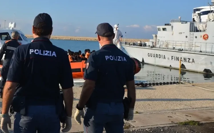 Agenti della Polizia di Stato osservano un'unità della Guardia di Finanza e un gommone con migranti in banchina al porto