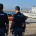 Agenti della Polizia di Stato osservano un'unità della Guardia di Finanza e un gommone con migranti in banchina al porto