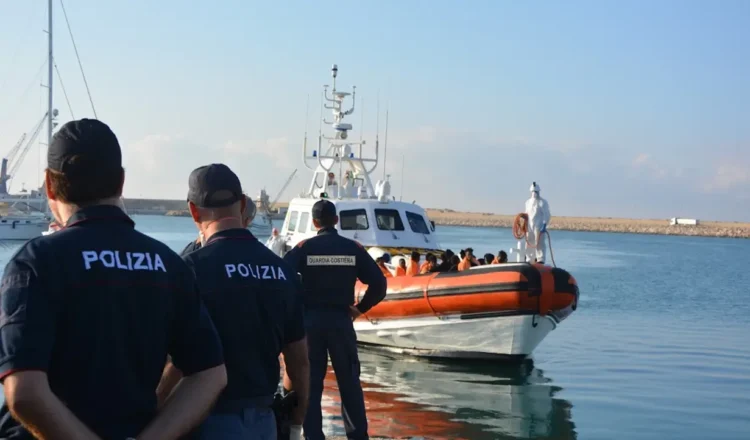 Agenti di polizia osservano una motovedetta della Guardia Costiera con migranti a bordo in un porto siciliano