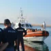 Agenti di polizia osservano una motovedetta della Guardia Costiera con migranti a bordo in un porto siciliano