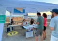 Gazebo dell'ASP di Ragusa su un lungomare affollato: due operatrici allo sportello accolgono cittadini per lo screening oncologico