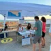 Gazebo dell'ASP di Ragusa su un lungomare affollato: due operatrici allo sportello accolgono cittadini per lo screening oncologico