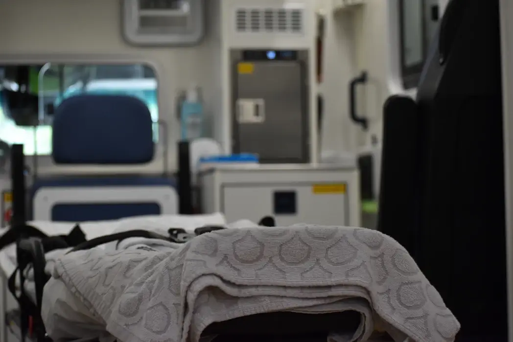 Barella con lenzuola ripiegate in un'ambulanza, sullo sfondo sfocato un sedile e apparecchiature sanitarie
