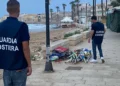 Due agenti della Guardia Costiera osservano un cumulo di ombrelloni e sdraio sequestrati sul lungomare di Scicli