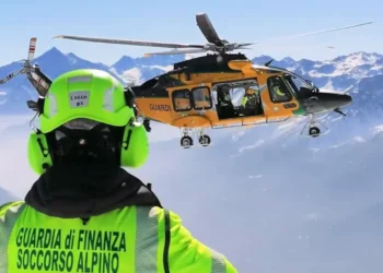 Soccorritore del Soccorso alpino della Guardia di Finanza osserva un elicottero in volo sopra le montagne innevate.