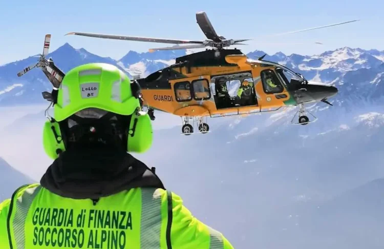 Soccorritore del Soccorso alpino della Guardia di Finanza osserva un elicottero in volo sopra le montagne innevate.