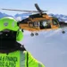 Soccorritore del Soccorso alpino della Guardia di Finanza osserva un elicottero in volo sopra le montagne innevate.
