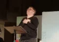 Amedeo Fusco recita in piedi davanti a un leggio durante uno spettacolo teatrale.