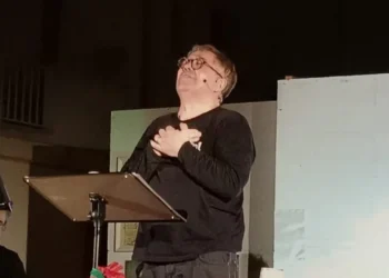 Amedeo Fusco recita in piedi davanti a un leggio durante uno spettacolo teatrale.