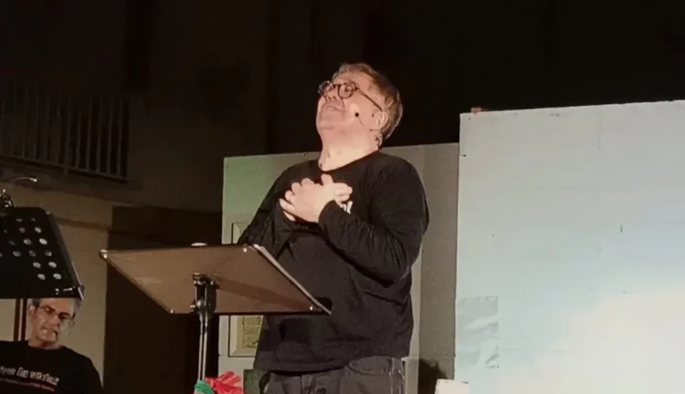 Amedeo Fusco recita in piedi davanti a un leggio durante uno spettacolo teatrale.