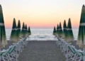 Ombrelloni chiusi e lettini allineati su una spiaggia libera al tramonto, mare sullo sfondo