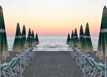 Ombrelloni chiusi e lettini allineati su una spiaggia libera al tramonto, mare sullo sfondo