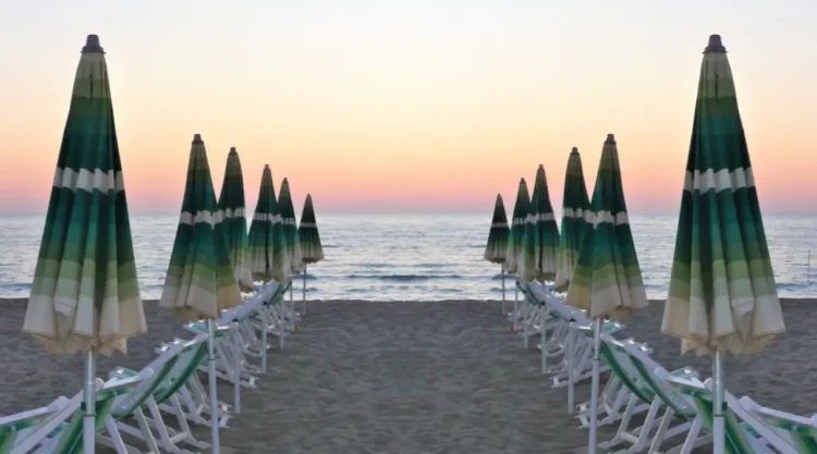 Ombrelloni chiusi e lettini allineati su una spiaggia libera al tramonto, mare sullo sfondo