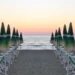 Ombrelloni chiusi e lettini allineati su una spiaggia libera al tramonto, mare sullo sfondo