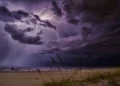 Temporale con fulmini sul mare al crepuscolo, cielo di nubi scure e una barca a vela in acqua vista dalla spiaggia