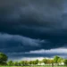 Nuvoloni scuri e minacciosi sopra un filare di alberi verdi e un campo aperto, poco prima di un temporale.
