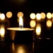 Candela accesa al buio con altre candele sfocate sullo sfondo, simbolo di lutto e raccoglimento