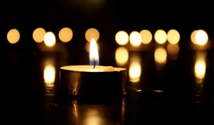 Candela accesa al buio con altre candele sfocate sullo sfondo, simbolo di lutto e raccoglimento