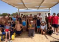 Ragazzi, famiglie e volontari in spiaggia davanti al gazebo della Base Nautica, uno su sedia a rotelle da mare