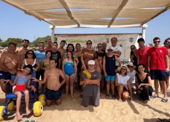 Ragazzi, famiglie e volontari in spiaggia davanti al gazebo della Base Nautica, uno su sedia a rotelle da mare