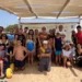 Ragazzi, famiglie e volontari in spiaggia davanti al gazebo della Base Nautica, uno su sedia a rotelle da mare