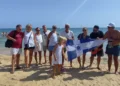Gruppo di soci in spiaggia con il gonfalone della Lega Navale Italiana, barche a vela sullo sfondo a Marina di Ragusa