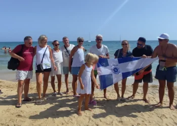 Gruppo di soci in spiaggia con il gonfalone della Lega Navale Italiana, barche a vela sullo sfondo a Marina di Ragusa