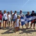 Gruppo di soci in spiaggia con il gonfalone della Lega Navale Italiana, barche a vela sullo sfondo a Marina di Ragusa