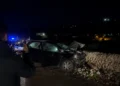 Auto incidentata di notte contro un muro a secco, un uomo la riprende con lo smartphone, luci blu dei soccorsi sullo sfondo