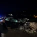 Auto incidentata di notte contro un muro a secco, un uomo la riprende con lo smartphone, luci blu dei soccorsi sullo sfondo