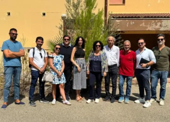 Gruppo di persone davanti a una villetta dell'ex base Nato di Comiso, edificio con intonaco degradato sullo sfondo