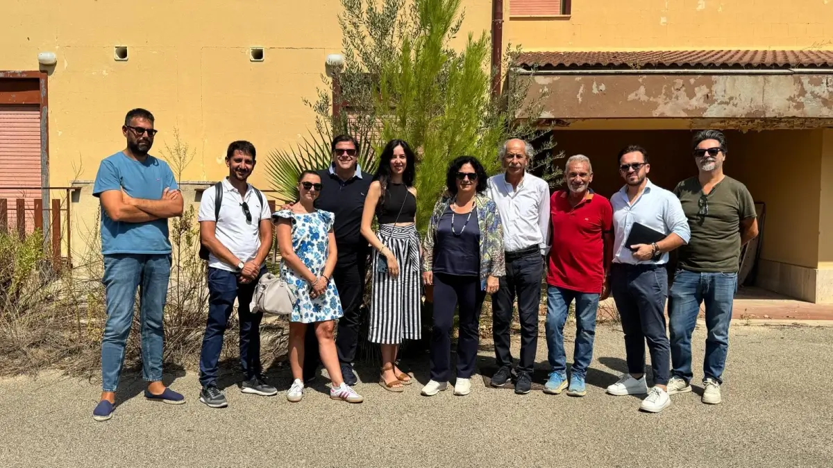 Gruppo di persone davanti a una villetta dell'ex base Nato di Comiso, edificio con intonaco degradato sullo sfondo