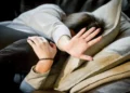 Donna sdraiata su un divano con il volto nascosto tra i capelli e una mano tesa in un gesto di rifiuto