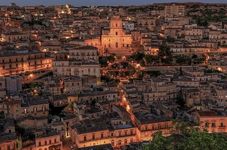 Veduta notturna del centro storico di Modica con il Duomo di San Giorgio illuminato tra le case.