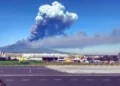Colonna di cenere e fumo dell'Etna in eruzione vista dall'area industriale di Catania, con lo scalo aeroportuale sullo sfondo