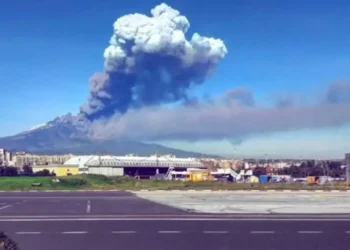 Colonna di cenere e fumo dell'Etna in eruzione vista dall'area industriale di Catania, con lo scalo aeroportuale sullo sfondo